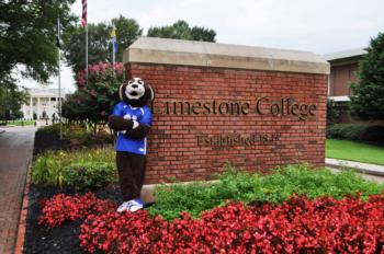 mascot beside limestone college sign and red flowers