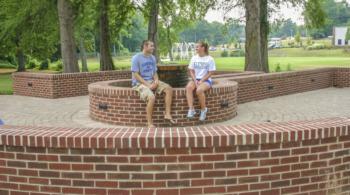 two students sitting on a brick structure in a park