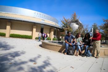 group of people near a building with a sphere sculpture