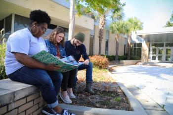 three students looking at a book outdoors