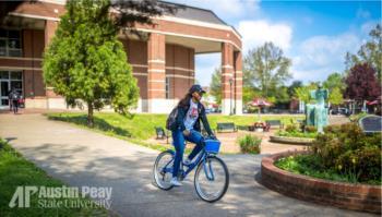 student biking past university buildings with 'AP Austin Peay State University'