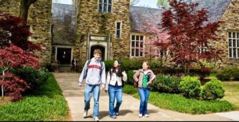 three students walking outside stone campus building