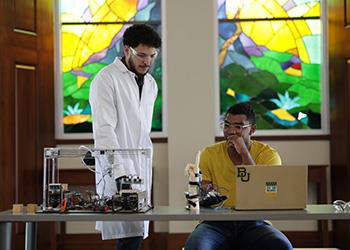 two students with electronics against stained glass window