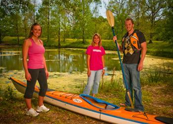 three people with a kayak near a pond in a park setting