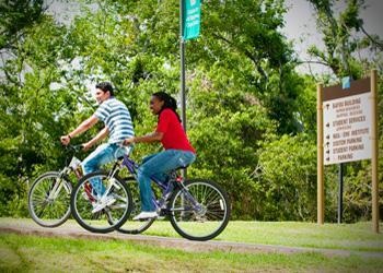 two people biking past a sign on a campus trail