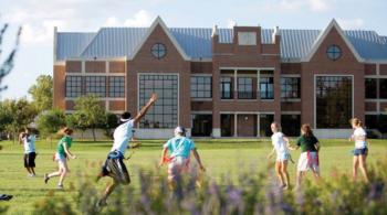 students playing frisbee in front of a campus building