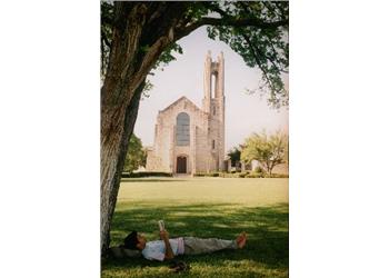 person relaxing under a tree with a building in background