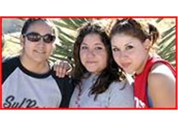 three women smiling with palm trees behind