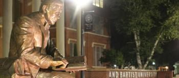 bronze statue of a person with book next to a sign