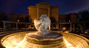 fountain with lit sculpture in front of a building at dusk