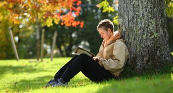 student reading under a tree in a lush setting