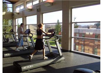 two people on treadmills in a gym with windows