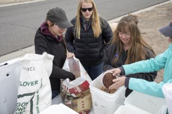 three people filling planting equipment from white bins