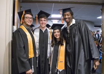 four graduates smiling in caps and gowns