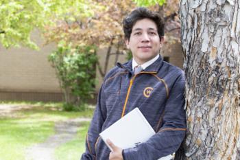 student standing by a tree holding a notebook