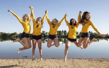 five students jumping by lake in yellow tops