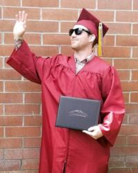 graduate waving in cap and gown with diploma