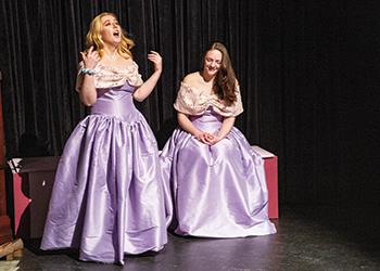 two women in purple dresses performing on stage