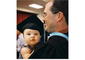 baby in graduation cap held by person in teal regalia