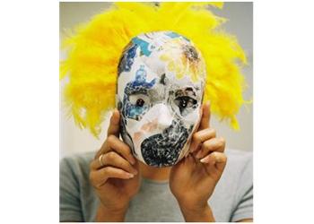 person holding a painted mask with yellow feathers