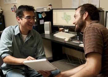 two men discussing over a document in an office