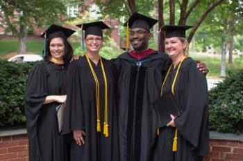 group of graduates in gowns and caps posing outdoors