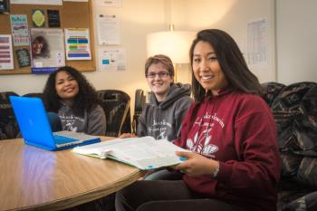 three students in maroon sweatshirts studying with laptop